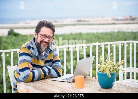 Homme barbu souriant, bras croisés assis à table Banque D'Images