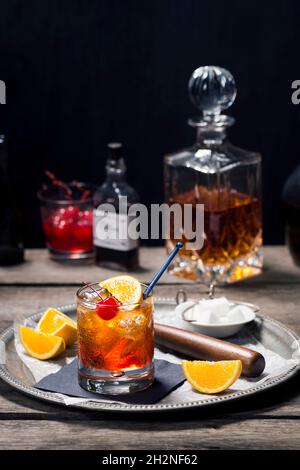 Cocktail à l'ancienne dans le verre Rocks avec ingrédients et outils de bar dans le bar en bois d'époque sombre Banque D'Images