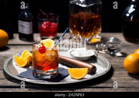 Cocktail à l'ancienne dans le verre Rocks avec ingrédients et outils de bar dans le bar en bois d'époque sombre Banque D'Images