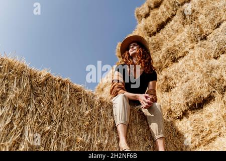 Femme portant un chapeau assis sur une haystack dans la ferme Banque D'Images
