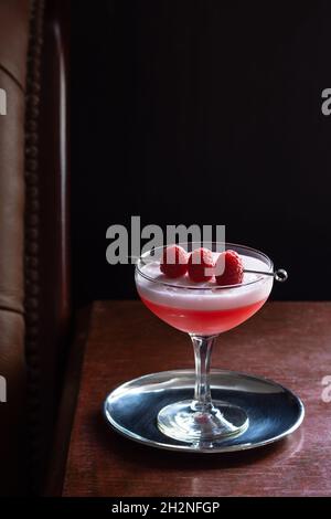 Cocktail Clover Club avec framboises et mousse blanche aux œufs en verre coupé dans un bar luxueux et sombre Banque D'Images