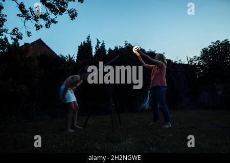 Fille regardant la lanterne lumineuse tenue par la grand-mère à travers le télescope à l'arrière-cour Banque D'Images