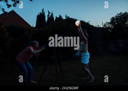 Grand-mère regardant la lanterne lumineuse tenue par une fille à travers le télescope pendant le coucher du soleil Banque D'Images