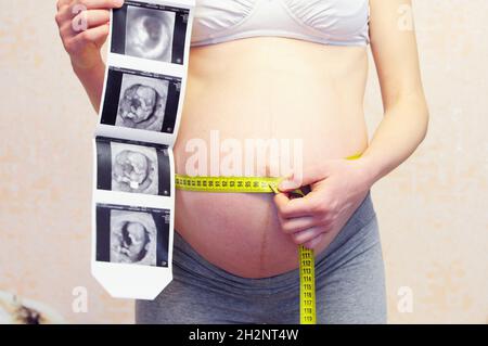 Échographie de grossesse.Femme enceinte tenant une échographie sur son ventre et son ruban de mesure.Grossesse chez les adolescentes.Concept de grossesse chez l'adolescent.Fermer Banque D'Images