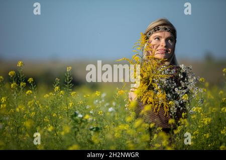 L'herboriste se tient dans un champ cultivé de colza et regarde en souriant. Banque D'Images