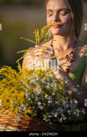 Une jeune femme savoure le parfum des herbes à fleurs.Verge d'or et hivernage communs. Banque D'Images