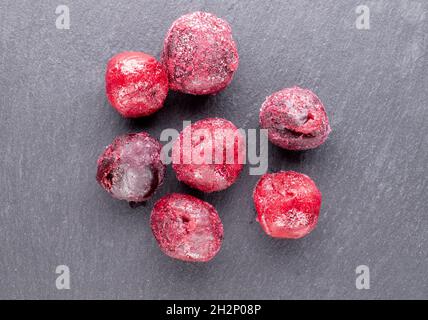 Plusieurs cerises rouges congelées parées bio sucrées sur un tableau d'ardoise, vue rapprochée, vue du dessus. Banque D'Images