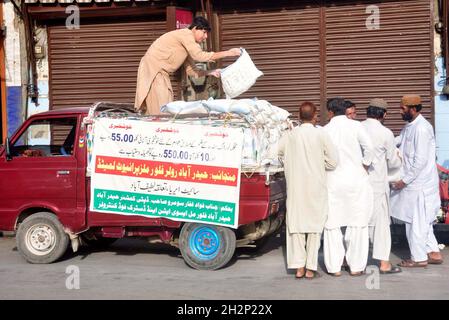 Les gens se rassemblent pour acheter des sacs de farine sur le prix des subventions d'un magasin de services publics mobiles vendu par le gouvernement de Sindh, comme le prix des articles généraux d'usage quotidien ont touché le ciel en raison de la hausse des prix dans le pays, au bord de la route à Hyderabad le samedi 23 octobre 2021. Banque D'Images