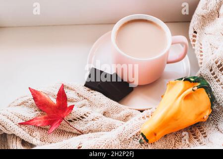 Une tasse de latte de café et des morceaux de chocolat, de citrouille jaune et de chandail tricoté sur le rebord de la fenêtre.Un automne chaud et confortable à la maison.Vue de dessus. Banque D'Images