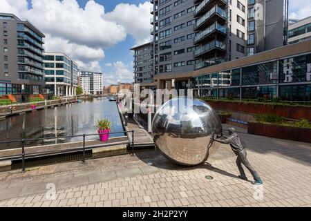 Une approche réfléchie - sculpture d'un garçon poussant une sphère réfléchissante à Clarence Dock, centre-ville de Leeds Banque D'Images