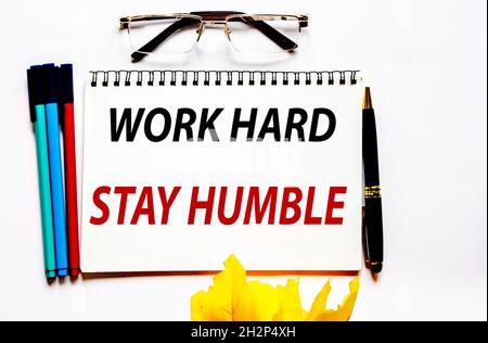 Travaillez dur, restez humble, le texte est écrit sur un bloc-notes blanc, des marqueurs et des lunettes sont à côté. Banque D'Images