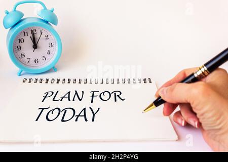 PLAN POUR AUJOURD'HUI, le texte est écrit sur un bloc-notes par la main d'une femme, sur un fond blanc.Il y a un réveil à proximité Banque D'Images