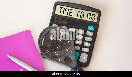 Le texte du temps de travail est inscrit sur l'écran de la calculatrice.Un ordinateur portable, un stylo, une loupe sont sur un fond blanc. Banque D'Images