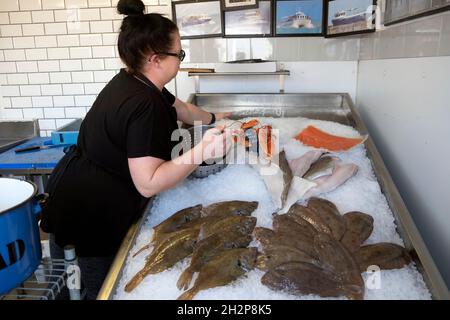 Femme travailleur vue arrière travaillant vendre du poisson frais sur glace à vendre dans la boutique de poissonniers de Dungeness Kent Angleterre KATHY DEWITT Banque D'Images