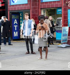 LONDRES, ANGLETERRE - octobre 19 2021: Les gens de Covent Garden attendent leurs amis, parcourant les nouvelles sur leur téléphone Banque D'Images