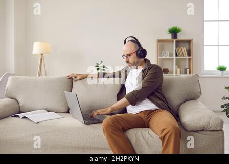 Adulte homme détendu écoutant de la musique avec un casque tout en travaillant sur un ordinateur portable à la maison. Banque D'Images