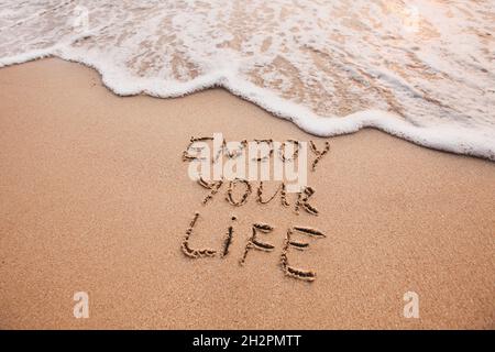 Profitez de votre vie, concept de bonheur, pensée positive, citation inspirée écrite sur plage de sable. Banque D'Images