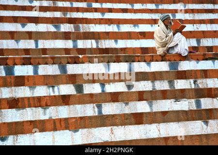 INDE.UN LIVRE EN MAIN, UN HOMME PRIE DEVANT LE GANGE SUR LES MARCHES DE KEDAR GHAT À VARANASI (BENARES) Banque D'Images