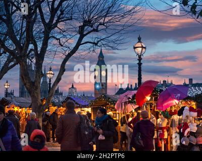 MARCHÉ DE NOËL DE LONDRES LES ACHETEURS DE SOUTH BANK ILLUMINENT LES étals DU marché de Noël DE WESTMINSTER South Bank et les acheteurs avec le Parlement derrière au crépuscule coucher du soleil Londres UK Banque D'Images