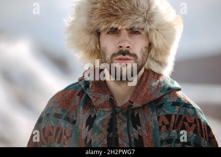 Portrait d'un bel homme hipster barbu dans un chapeau de renard arctique et un poncho Banque D'Images