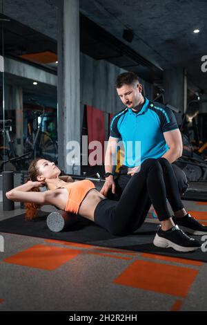 jeune femme se détendant avec un rouleau de relâchement myofascial avec entraîneur dans la salle de gym Banque D'Images