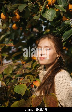 Une jeune femme prenant un persimmon dans le jardin d'automne, récolte Banque D'Images