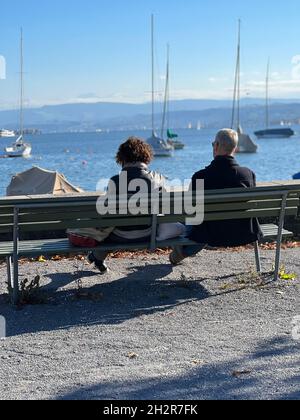 Zurich, Suisse 10 23 2021 couple hétérosexuel d'âge moyen assis sur un banc en bois observant le lac de Zurich avec des yachts. Vue arrière. Banque D'Images