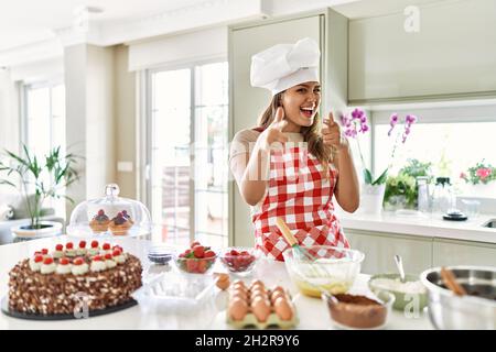 Belle jeune brunette pâtissière chef femme cuisant des pâtisseries à la cuisine en pointant les doigts vers l'appareil photo avec le visage heureux et drôle. Bonne énergie et vibes Banque D'Images