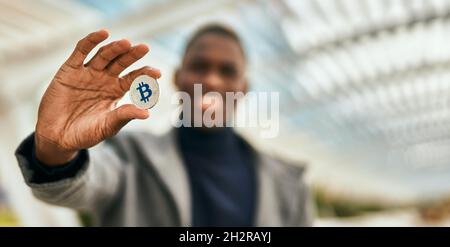 Un jeune homme afro-américain souriant se réjouit de tenir le bitcoin à la ville Banque D'Images
