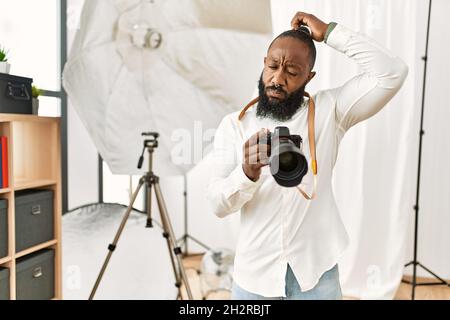 Photographe afro-américain, homme travaillant au studio de photographie, qui ne sait pas s'interroger sur la question. Incertain avec doute, pensant main sur la tête Banque D'Images