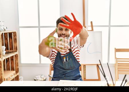 Jeune artiste arabe homme souriant heureux de montrer les mains peintes au studio d'art. Banque D'Images