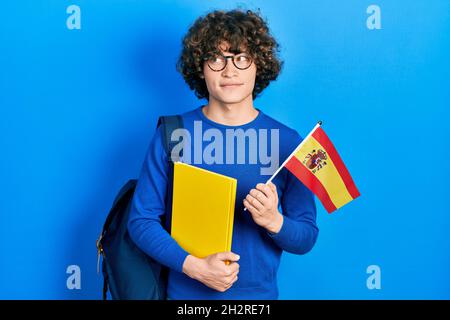 Beau jeune homme d'échange étudiant tenant le drapeau espagnol souriant regardant sur le côté et regardant loin de penser. Banque D'Images