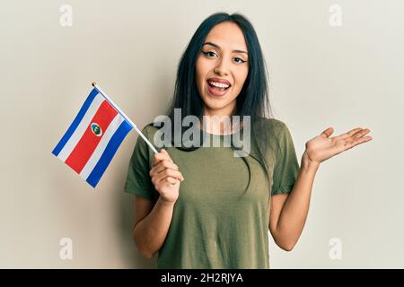 Jeune fille hispanique portant le drapeau du costa rica célébrant l'accomplissement avec un sourire heureux et l'expression du gagnant avec la main levée Banque D'Images