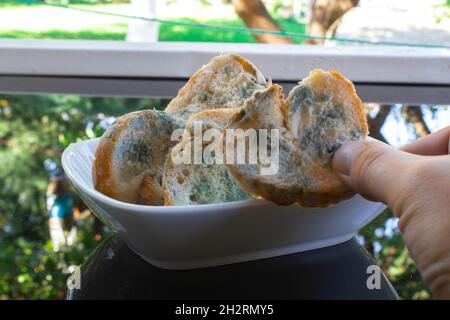 Homme main tenant quelques tranches de pain moulées dans une plaque en céramique blanche.Les aliments sont périmés et gaspillés Banque D'Images