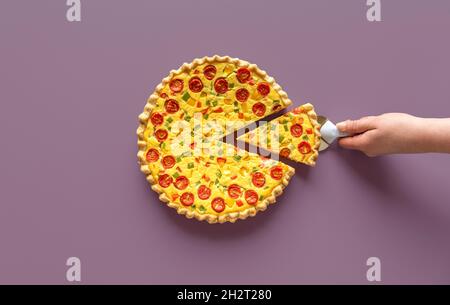 Main de femme prenant une tranche de quiche, vue de dessus.Quiche maison à la ricotta et aux légumes sur fond violet. Banque D'Images