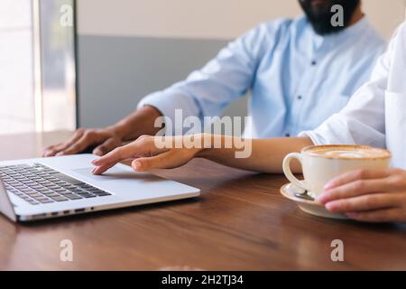 Gros plan sur des mains d'un homme d'affaires et d'une femme méconnaissable travaillant avec un ordinateur portable assis à une table dans un café, avec un doigt sur le pavé tactile. Banque D'Images