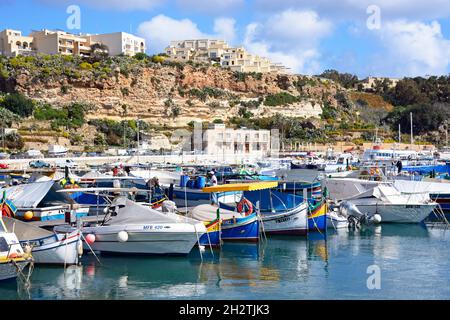 Vue sur les bateaux de pêche traditionnels maltais Dghajsa et les bateaux modernes dans le port avec des appartements sur la colline à l'arrière, Mgarr, Gozo, Malte. Banque D'Images