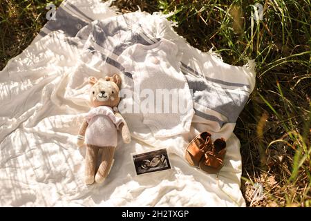 Petits vêtements de bébé faits main.Photo de l'échographie. Vêtements nouveau-nés sur fond beige avec herbe Banque D'Images