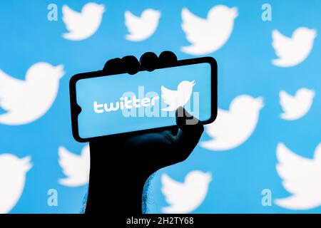 Smartphone avec le logo de réseau social Twitter sur l'écran dans une main trempée sur l'arrière-plan des logos Twitter Banque D'Images