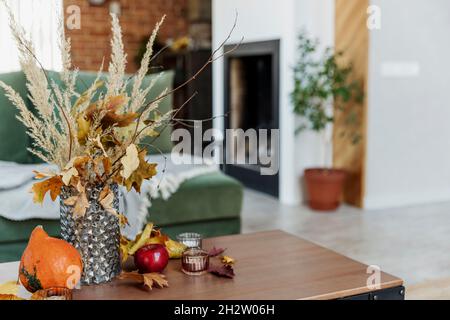 Décoration intérieure automnale.Bouquet de fleurs jaunes dans vase en verre sur table élégante en bois, citrouille, pommes rouges, feuilles, bougies,couverture.Gree Banque D'Images