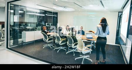 Femme d'affaires créative donnant une présentation dans une salle de réunion.Femme d'affaires confiante présentant des données financières à ses collègues dans un lieu de travail moderne Banque D'Images