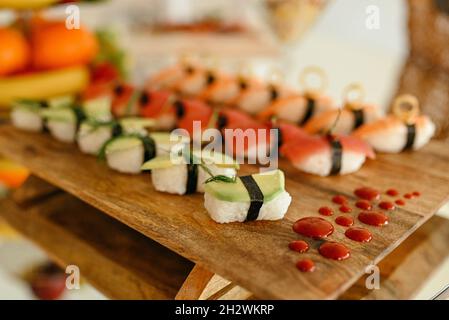 Ensemble de différents types de petits pains à sushis avec saumon, crevettes et légumes sur une assiette en bois Banque D'Images