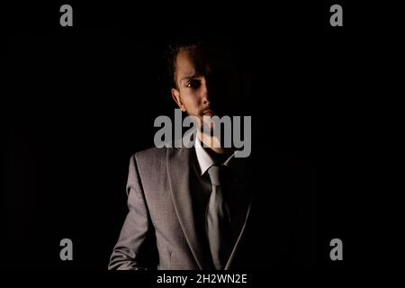 Un jeune homme d'affaires dans un costume gris élégant regardant la caméra avec éclairage moody qui jette la moitié de lui dans l'ombre Banque D'Images