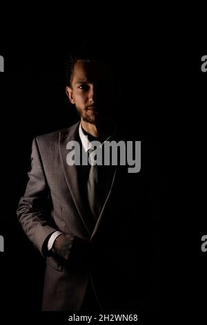 Un jeune homme d'affaires dans un costume gris élégant regardant la caméra avec éclairage moody qui jette la moitié de lui dans l'ombre Banque D'Images