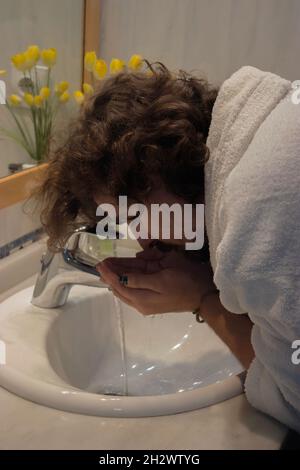 Un jeune homme en peignoir lave son visage dans son lavabo avant de se raser.Home Spa concept Beauté concept. Banque D'Images