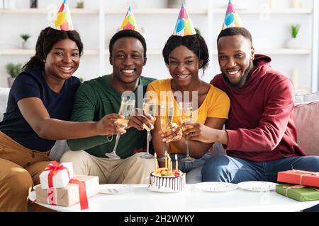 Joyeux jeunes noirs célébrant leur anniversaire à la maison, buvant du champagne Banque D'Images