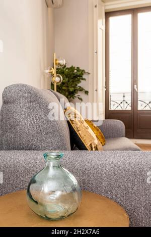 Récipient décoratif en verre sur une table basse en bois à côté d'un canapé gris dans l'appartement de location de vacances Banque D'Images