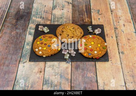 Plateau en ardoise noire avec biscuits et copeaux de chocolat colorés sur une table en bois Banque D'Images