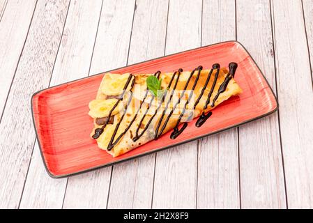 Crêpe fourrée de chocolat et de bananes arrosée de sirop de chocolat à la menthe sur une assiette rouge Banque D'Images