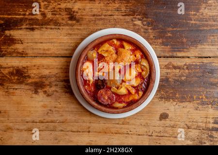 Tapas espagnoles de tripe à la madrileña avec chorizo, bacon et saucisse de sang dans une casserole d'argile sur table en bois Banque D'Images